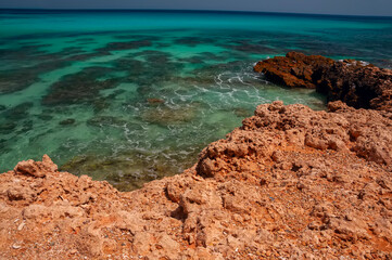 Beach with emerald water and wild red rocky shore. 
