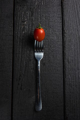 A fork with a tomato on it on a black table.