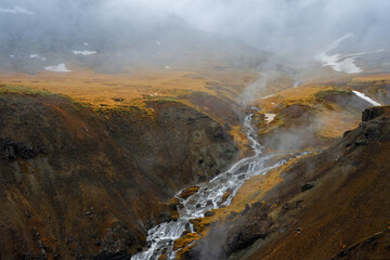 montagne ocre avec une rivière d'eau chaude du fait de la géothermie coulant en son sein nuage et vapeur Paysage islandais