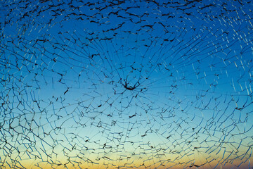 Dark blue broken shattered glass with black cracks and yellow orange sunset on background