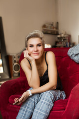 Obraz premium Blonde businesswoman in black top with mobile phone in hand sitting on red sofa