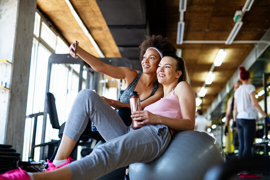 Happy fit women, friends smiling, talking and taking photos after work out in gym. Social media.
