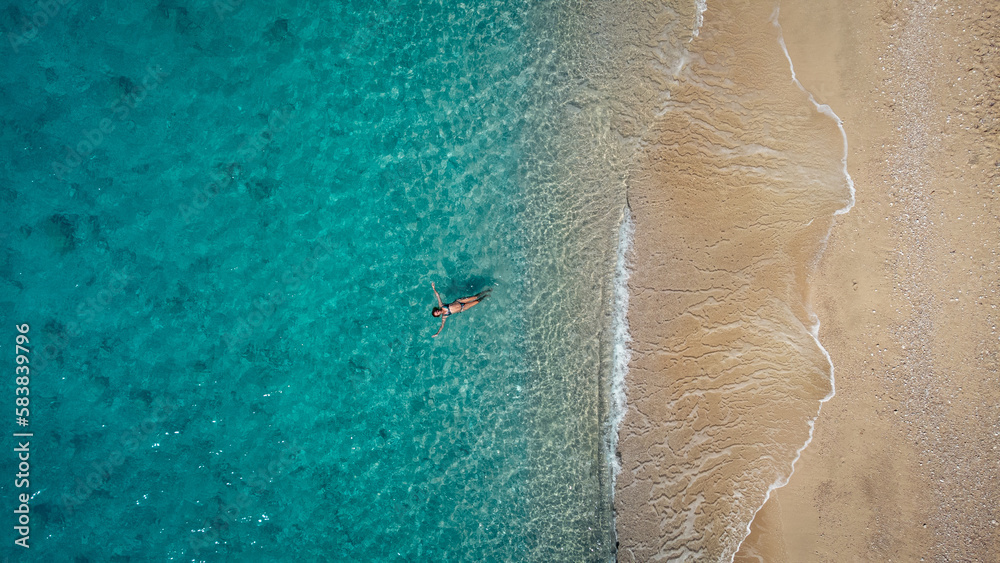 Wall mural aerial view of beautiful happy woman in swimsuit laying in the shallow sea water, enjoying sandy bea