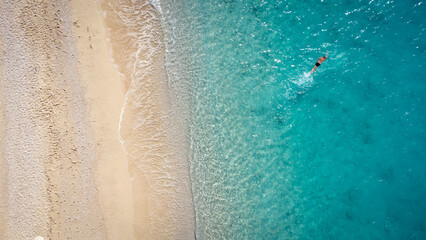 Fototapeta na wymiar Aerial view of man swimming in the shallow sea water, enjoying beach and soft turquoise ocean wave. Tropical sea in summer season on Egremni beach on Lefkada island.