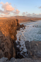 Fototapeta na wymiar Vista panorámica de la playa de Playa del Castillo desde los acantilados de la playa de arena dorada y el mar turquesa durante la puesta de sol con cielo azul claro en Fuerteventura.