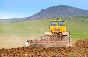 Fototapeta premium Traktok plows the land, preparing for sowing seeds. Industrial agriculture and farming. Tractor driver at work in the field. Harvesting, harvester harvests.