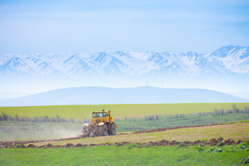 Fototapeta premium Traktok plows the land, preparing for sowing seeds. Industrial agriculture and farming. Tractor driver at work in the field. Harvesting, harvester harvests.