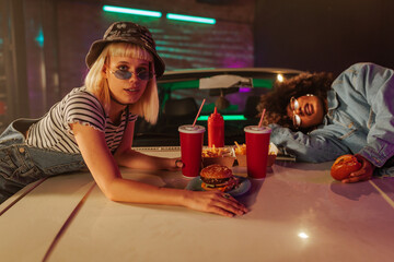 Cool girls eating takeout on car hood.