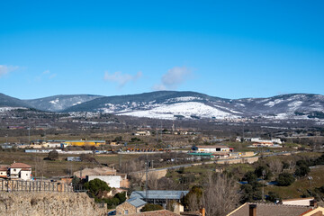Fototapeta na wymiar Paisaje del pueblo madrileño Buitrago de Lozoya con las montañas nevadas al fondo bajo un cielo soleado en un frío día de primavera.