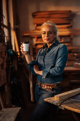 Fototapeta na wymiar Trendy female carpenter drinking coffee in workshop.