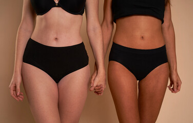 Two unrecognizable women in black underwear standing and holding hands