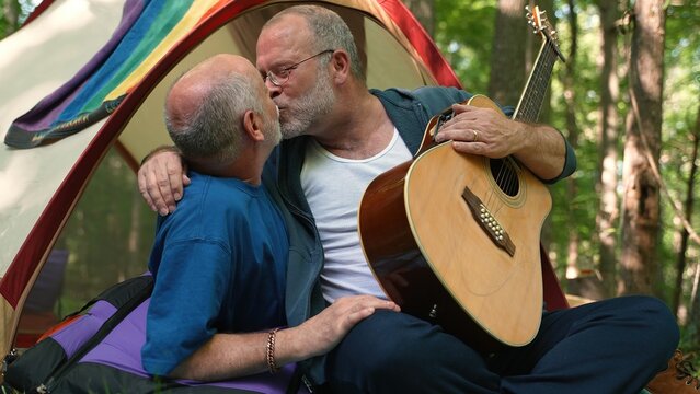 Closeup of two gay men in a tent with pride flag holding each other and kissing showing affection.