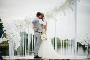 The bride and groom kissing. Newlyweds with a bouquet standing on wedding ceremony under the arch...