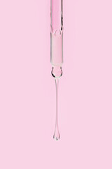 Glass pipette with facial serum and falling drop on light pink background. Liquid skin care cosmetic product with bubbles closeup. Serum with retinol in droplet. Essential oil or gel macro.