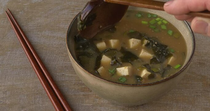 Scooping miso soup with kombu dashi, tofu, wakame seaweed and scallions with wooden spoon.