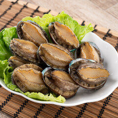 Delicious raw abalone in a plate on wooden table background.