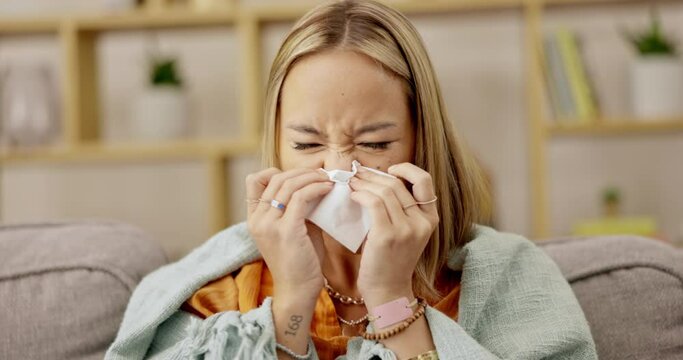 Sick, sneeze and woman blowing nose with flu, cold or fever while in a home, house or apartment to recover on couch. Sofa. Mexico and person ill with virus or bug while covered in a blanket