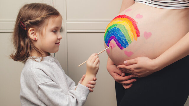 Sweet little daugter painting pregnant belly her mother. Pregnant mom and her child having fun together at home. Family, healthy pregnancy and baby birth.