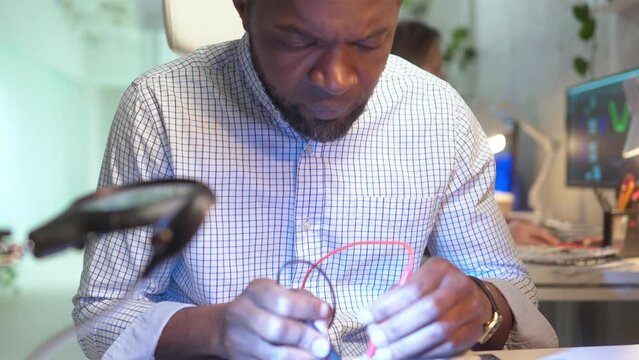 Close-up portrait of focused young worker of modern company fixing computer microscheme diagnostic with multimeter. Bearded African-American man using tester on motherboard in modern office.