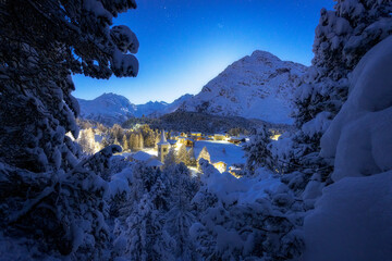 Fairy tale view of Chiesa Bianca covered with snow on a winter starry night, Maloja, Bregaglia, Engadine, Canton of Graubunden, Switzerland