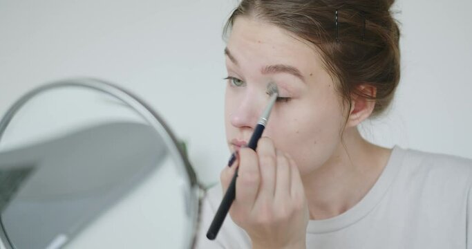 A young woman paints her eyelids and looks at herself in the mirror. Care for the female skin of the face. Makeup for a girl. A beautiful girl paints her eyes. High quality 4k footage