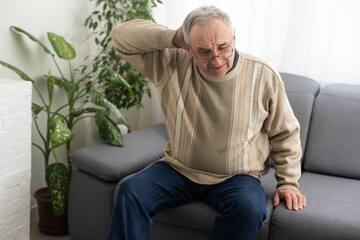 Fototapeta premium Senior man having headache and touching his head while suffering from a migraine in the living room, Mature man presses a hand to head suffers from unbearable pain.