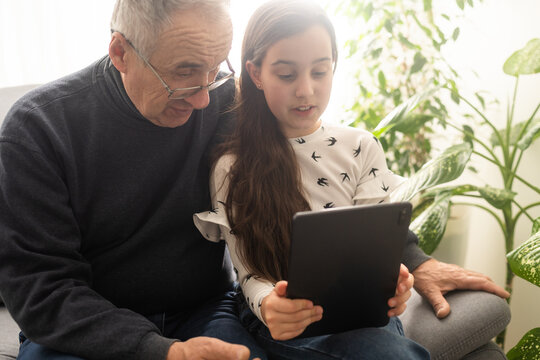 Happy family senior grandfather and girl watching cartoon on tablet on weekend day at home together