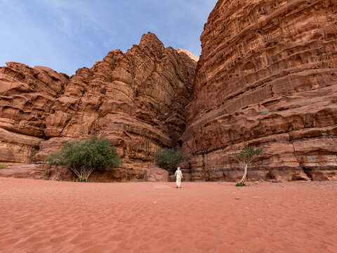 A beduin with traditional white clothes walking towards a canyon in Wadi Rum desert, UNESCO World Heritage Site, Jordan