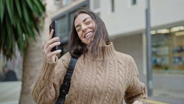 Young beautiful hispanic woman using smartphone dancing at street