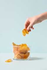 Child hand take organic jackfruit chips from glass jar on blue background. Fruits chips for vegan with antioxidant, vitamin from tropical island Ceylon. Vertical format.