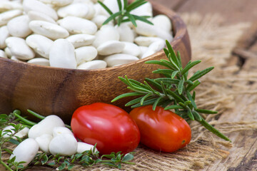 white beans, tomatoes and herbs on wooden background