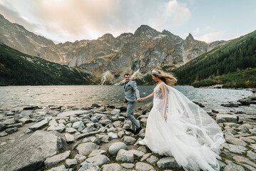 The bride and groom near the lake in the mountains. A couple together against the backdrop of a mountain landscape. Morskie Oko (Sea Eye) Lake. Tatra mountains in Poland. - obrazy, fototapety, plakaty