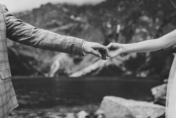 View on hands. Newlyweds together hold hands. Romantic wedding couple in love standing on the background lake in the mountains. Black and white photo.