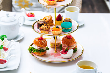 Afternoon tea and sweets on the table,English afternoon tea in garden cafe: scones with cream and strawberry jam with various sandwiches on selective focus background.