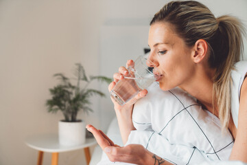 Side portrait of blonde woman taking her morning vitamins while still in bed 