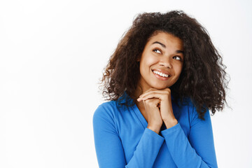 Fototapeta na wymiar Portrait of beautiful young Black woman smiling, looking happy and carefree, daydreaming, standing in casual clothes over white background