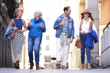 Four active seniors enjoy a leisurely stroll through quiet city streets, chatting and laughing as they explore the urban landscape.