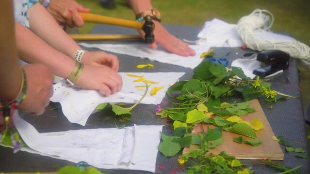 close up hands of a child and adults placing different leaves and flowers on a piece of cloth to hit it with a hammer to creating interesting looking images family activity playground for kids
