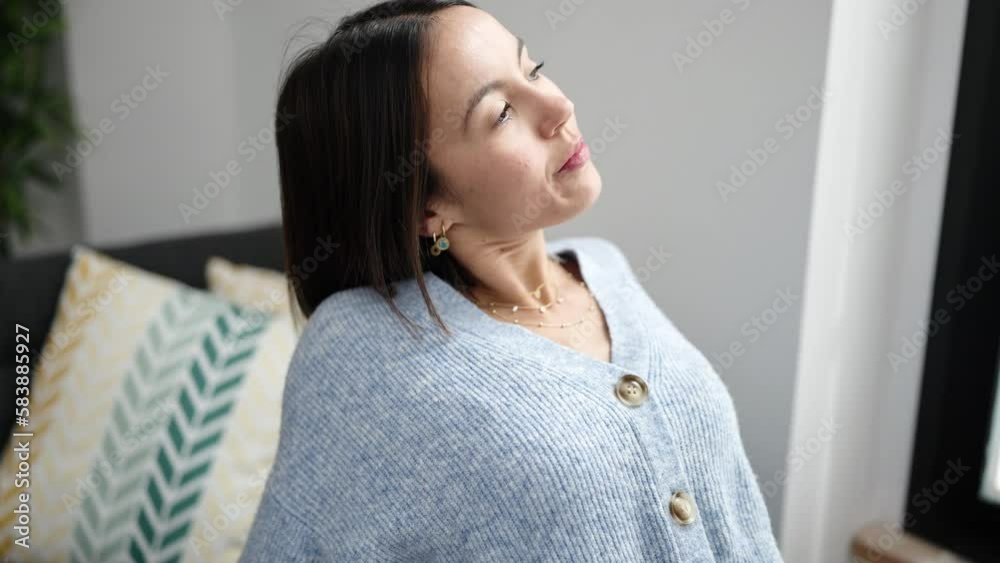 Sticker young beautiful hispanic woman sitting on sofa stretching arms at home