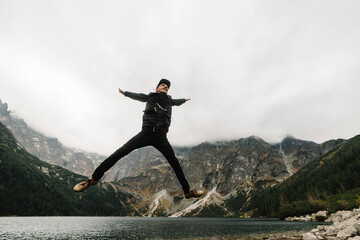 A man jumping on the stony shore of the Sea Eye lake in Poland. Scenic mountain view. Morskie Oko. Tatra mountains.