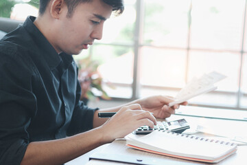 Young businessman in black shirt calculating his bill by using a calculator, thinking about his financial information and debt problems, want to reduce expenses and save money.