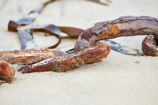 Mousehole, Cornwall, UK - old rusty chain half buried in sand of low tide harbour