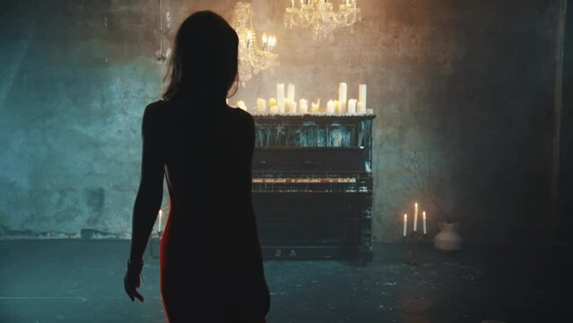 Rear view dark shadow mystery silhouette fantasy lady gothic woman blond hair in red dress walks in black room piano candles light burn. Evening gown open bare back fashion model sexy girl vampire. 4k