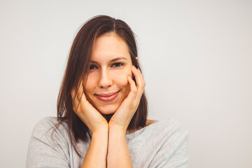 Portrait of young woman holding hands on her face with a sbtle smile looking at the camera on white background 