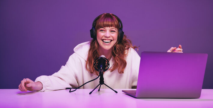 Happy young woman laughing while recording a live radio show in a studio