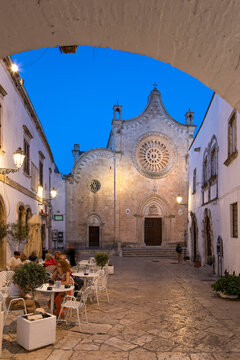 Cattedrale Santa Maria Assunta cathedral in the Largo Arcid Teodoro Trinchera square and cafe floodlit in evening, Ostuni, Brindisi province, Puglia
