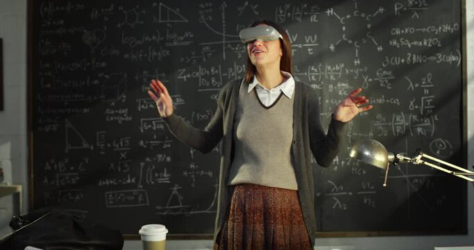 Portrait of Young Teacher in University Classroom Using VR Mask In Front of Blackboard with Mathematic Formulas. Science Female Researcher in Using Technology, Solving Equations in the Metaverse
