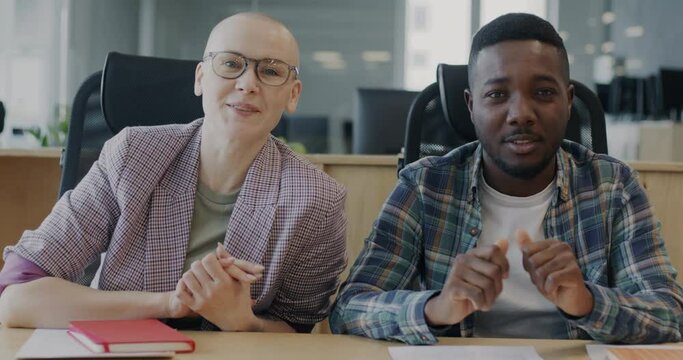 Man and woman colleagues making online video call speaking and smiling looking at camera in shared office. Communication and coworking concept.