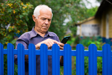 Elderly man writes message on smartphone. Concept of using digital gadgets by elderly