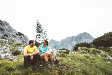 Mountaineering couple sitting down on the grass having a break from hiking a beautiful trail in the summer Alps 